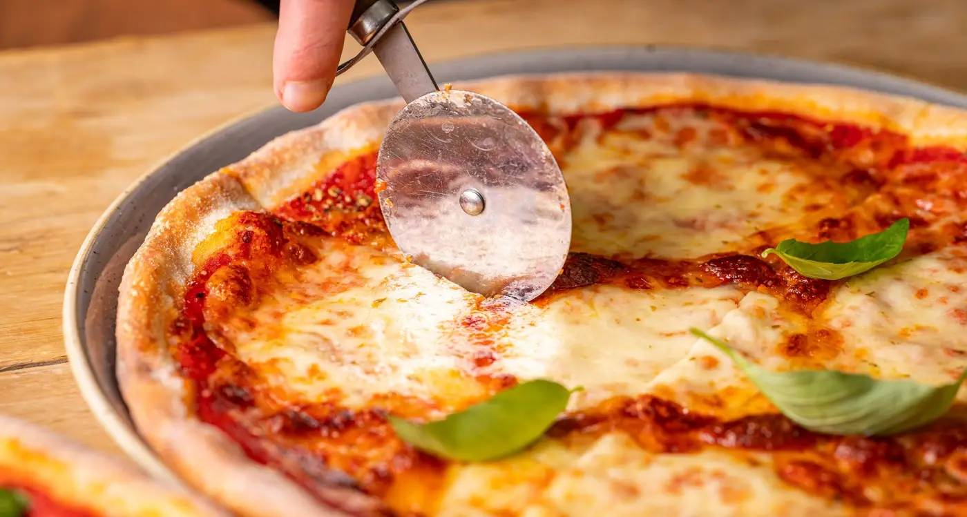 Wildwood Restaurants margherita pizza being sliced into, topped with basil leaves