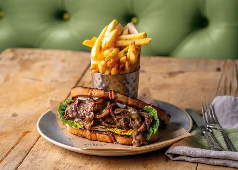 Wildwood Restaurants Philly cheesesteak sandwich, succulent marinated steak strips, chimichurri dressing, fried onions, cheese, mayo, grilled sourdough bread